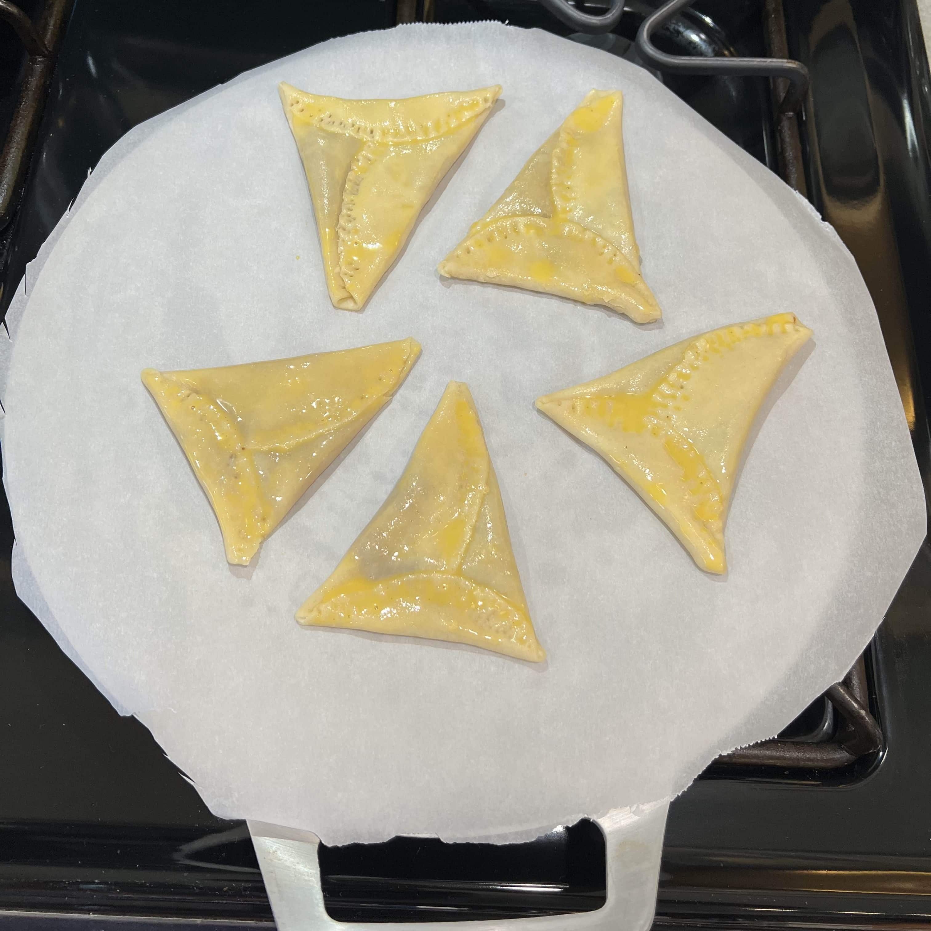 Unbaked triangular pine tarts brushed with egg wash on a baking sheet